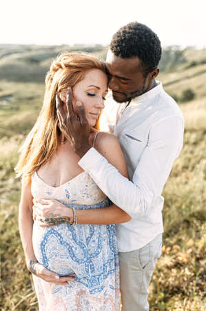 A portrait of multiethnic couple in love, they are looking forward a baby. A handsome black guy is hugging his beautiful pregnant wife and touching her face tenderlyの写真素材