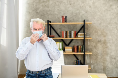 Senior man in smart casual wear with a protection medical mask on the face in the contemporary officeの写真素材