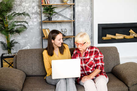 An adult granddaughter teaches a gray-haired modern grandmother how to use a laptopの写真素材