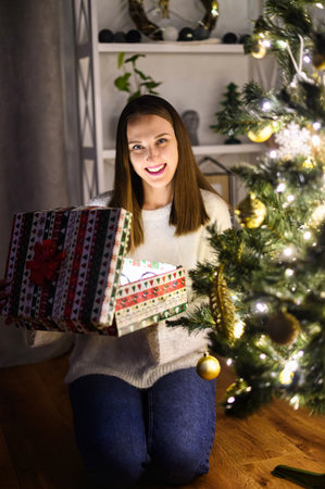 A young woman with a gift box near Christmas treeの写真素材