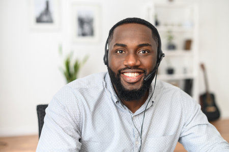 Smiling young African-American office worker wearing a headset and looking at the camera, a positive...