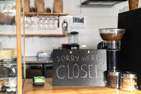 Closed sign board on the bar counter in an empty coffee shop. Cafe, bar closed due outbreak lockdown. Small business crisis conceptの写真素材
