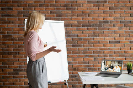 A confident female business coach, tutor conduct webinar, online training. A middle-aged woman...