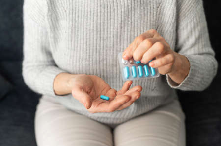 Top view of female hand holding a blue prescription pill and a blister pack, close-up of a palm of a senior lady with a tablet, taking medication or supplements for stronger immune systemの写真素材