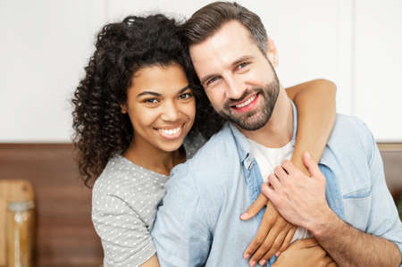Close-up portrait of happy multi-ethnic couple in love. An African woman hugs a caucasian guy from...
