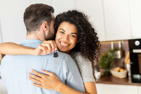 Charming and glad African-American woman holds keys in embraces of a guy. Happy interracial couple moved in new house, buying a real estateの写真素材