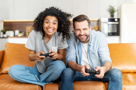 A multiracial couple enjoys time playing video game on the console, excited and tense young African...