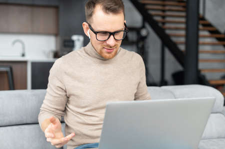Young employee with glasses, sitting at the laptop on a business meeting, feeling not very well so working on a distance, talking with potential clients and partners, looking at the laptop screenの写真素材