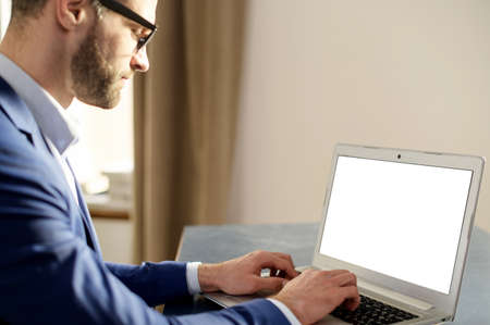 Busy successful young bearded hipster guy in glasses and formal wear sitting at the desk in home...