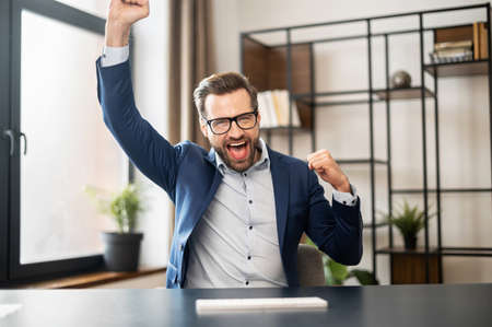 Successful lucky young bearded businessman in formal wear raised fists up celebrating success, screaming yes, passed test with high score, got promoted, won lottery, closed a deal. Victory conceptの写真素材