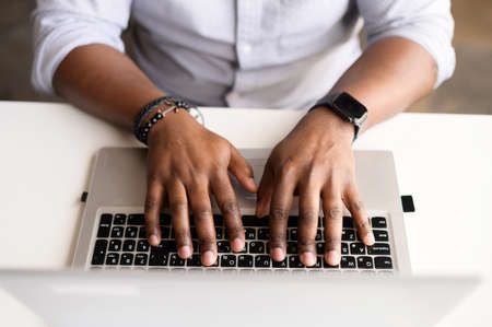 A male hands on the laptop keyboard. Top view an African-American guy is typing email, programmer is develops software, cropped photo, a face is not visible, close-up pictureの写真素材