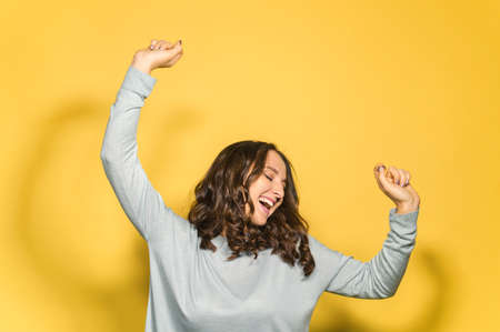 Carefree young woman is dancing isolated on yellow background, smiling and happy female feels freedom, raised arms up and feels the music beats, enjoying dancing aloneの写真素材