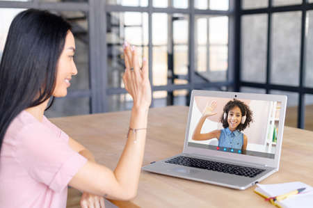 Woman teacher has video lesson, greets school-age African girl in headset, new education system, explaining, enjoying studying online or communicating with school professor via video call at homeの写真素材