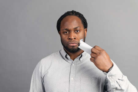 African-American man with a sealed mouth with a scotch tape taking tape off, fights against racism and for their rights, a black guy has the right to vote, isolated on greyの写真素材