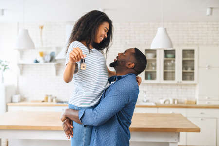 Hilarious African-American young couple celebrating buying a property, excited man carrying cheerful...