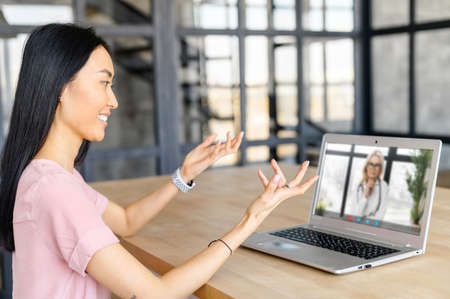 An Asian woman uses a laptop to communicate with her doctor during quarantine, remote video consultation on the computer screenの写真素材