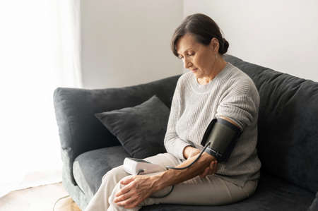 Senior woman checking blood pressure level at home, older female suffering from high blood pressure...