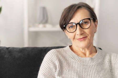 Charming middle aged woman wearing stylish eyeglasses looks at the camera with a calm friendly...