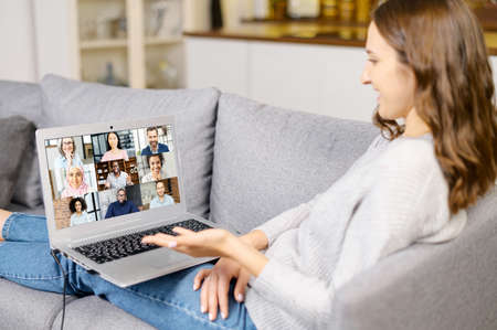 Young woman using a laptop computer for video connection with diverse group of people, female...