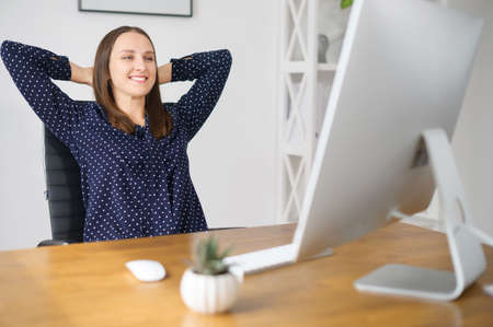 Smiling female employee takes a break on the workplace in the office, leaned back in the chair rests...