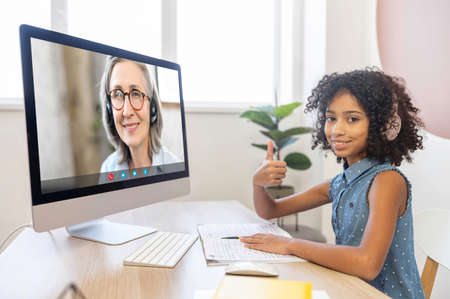 Cute multiracial girl studying on the distance, watching online classes on the PC computer, a senior...