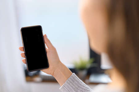 Back view at an empty smartphone screen in hand of a woman, woman holds a mobile phone with blank display, mockup, copy spaceの写真素材