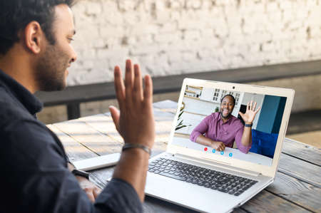 Two male colleagues greeting each other during video meeting. Multiracial business partners involved virtual conference. Back view male student takes an online language classes from African teacherの写真素材