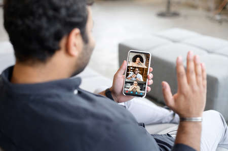 Back view on the smartphone in hand of male, phone screen with a several people talking together in same time, guy is using mobile app for video call, video connection with friends or colleaguesの写真素材
