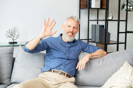 Video connect with modern mature grey-haired man, he waving and greeting, talks and speaks with...