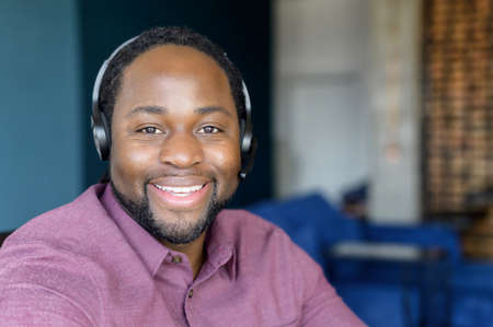 Call center operator wearing headset looks at the camera with cheerful smile, headshot of cheerful African-American man in headset, technical support worker in headphones in touchの写真素材