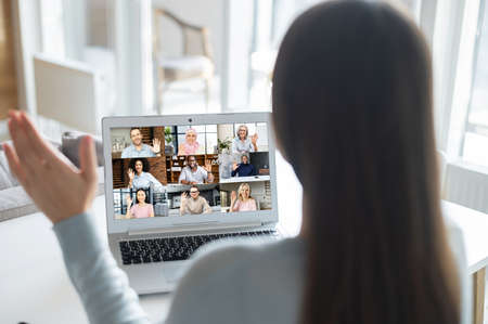 View from back on a woman using laptop for video connection. Virtual conference with a group of diverse people, multiracial team greeting each other online, video call to coworkers on the distanceの写真素材