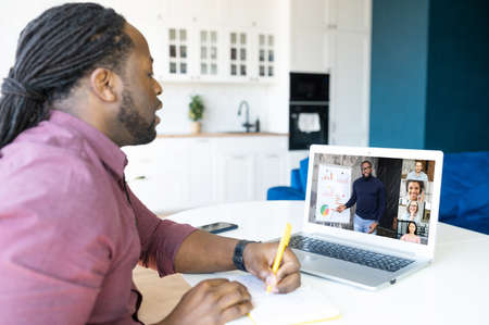Focused African-American male student with locks hairstyle using laptop computer for studying on the...