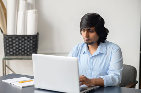 Indian man in smart casual shirt using laptop indoor, concentrated hindu male office employee typing, sends emails, working on a new project, researches the topic, develops strategies, websurfingの写真素材