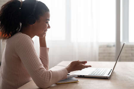 Side view a multiracial young woman wearing headset holding video meeting, talking with colleagues...