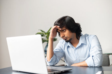 Exhausted and upset indian businessman looks at the laptop screen with disappointment, overworked...