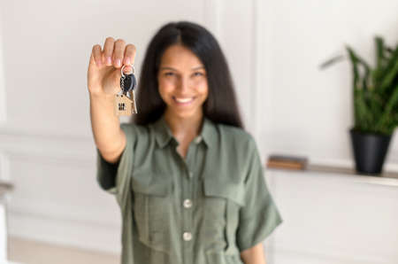 Selective focus on the key in hand of happy young indian woman, cheerful female moved in new house, rent apartment, bought own real estate, the key with keyring in shape of little houseの写真素材