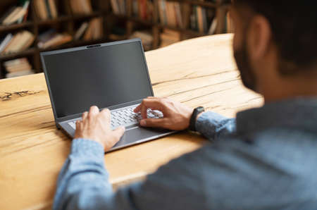 Indian bearded man using laptop with blank screen, using new computer app, back view, copy space for advertising, promotion, copy spaceの写真素材