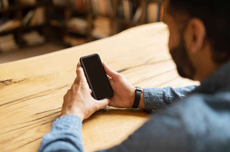 Indian bearded man holding a black mobile phone with blank screen, using new mobile app, male hand...