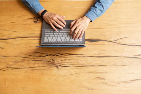 View from the top at businessman hands are typing and using laptop keyboard, researching, web surfing, sending and answering emails, on the wooden deskの写真素材