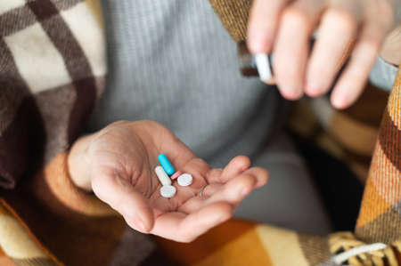A hand of senior woman holds different tablets and pills, close-up medicines on the female palm. Treatment concept, vitamins for elderly people for healthy and wellnessの写真素材