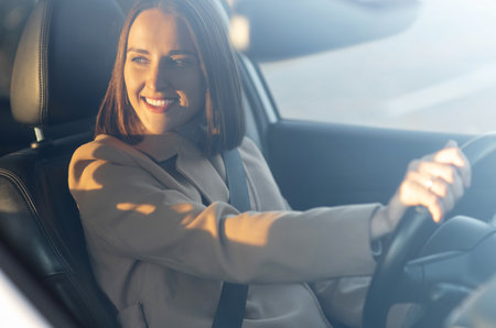Cheeeful young woman is driving a car. Happy lady smiling and holds hands on a steer wheel, enjoying...