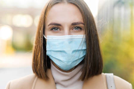 Close-up portrait of woman wearing protective medical mask looks at the camera. Protect yourself...