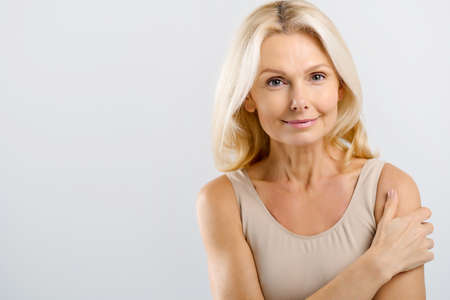 Good-looking beautiful middle-aged woman posing in studio over grey background. Charming mature lady...