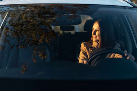 Cheerful woman driving a car and smiling. Young success happy brunette woman is driving a car. Lady...