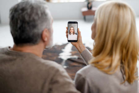Middle-aged mature parents talking with a grown daughter on the distance, mature couple using smartphone for video connection with a family psychologist. Social distancing conceptの写真素材