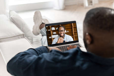 African-American man taking online language classes, online teacher on laptop screen. Two male multiracial employee talking online, discussing business tasks on the distance, friends chatting onlineの写真素材