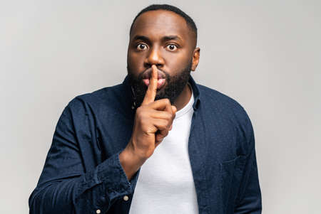 Keep the silence. African-American guy holding index finger near lips in shh gesture, calls to be quieter, keep a private secret, hush and do not talkingの写真素材