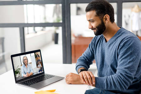 Indian male student studying online, watching webinar holding female teacher, other students...