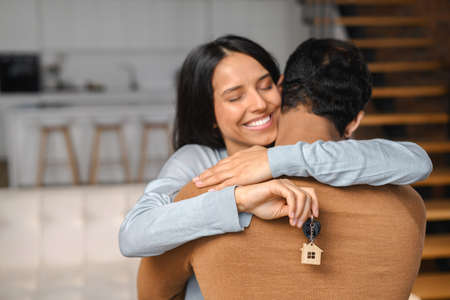 Focus on the keys in the hand of young wife, husband is hugging her. Married young Indian couple buy a real estate. Multiracial family excited about relocation to new house, happiness conceptの写真素材