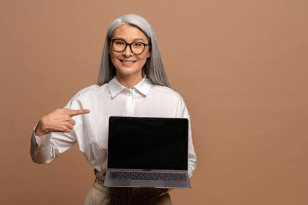 Look at advertisement. Happy elegant woman employee pointing laptop blank display, mock up empty...